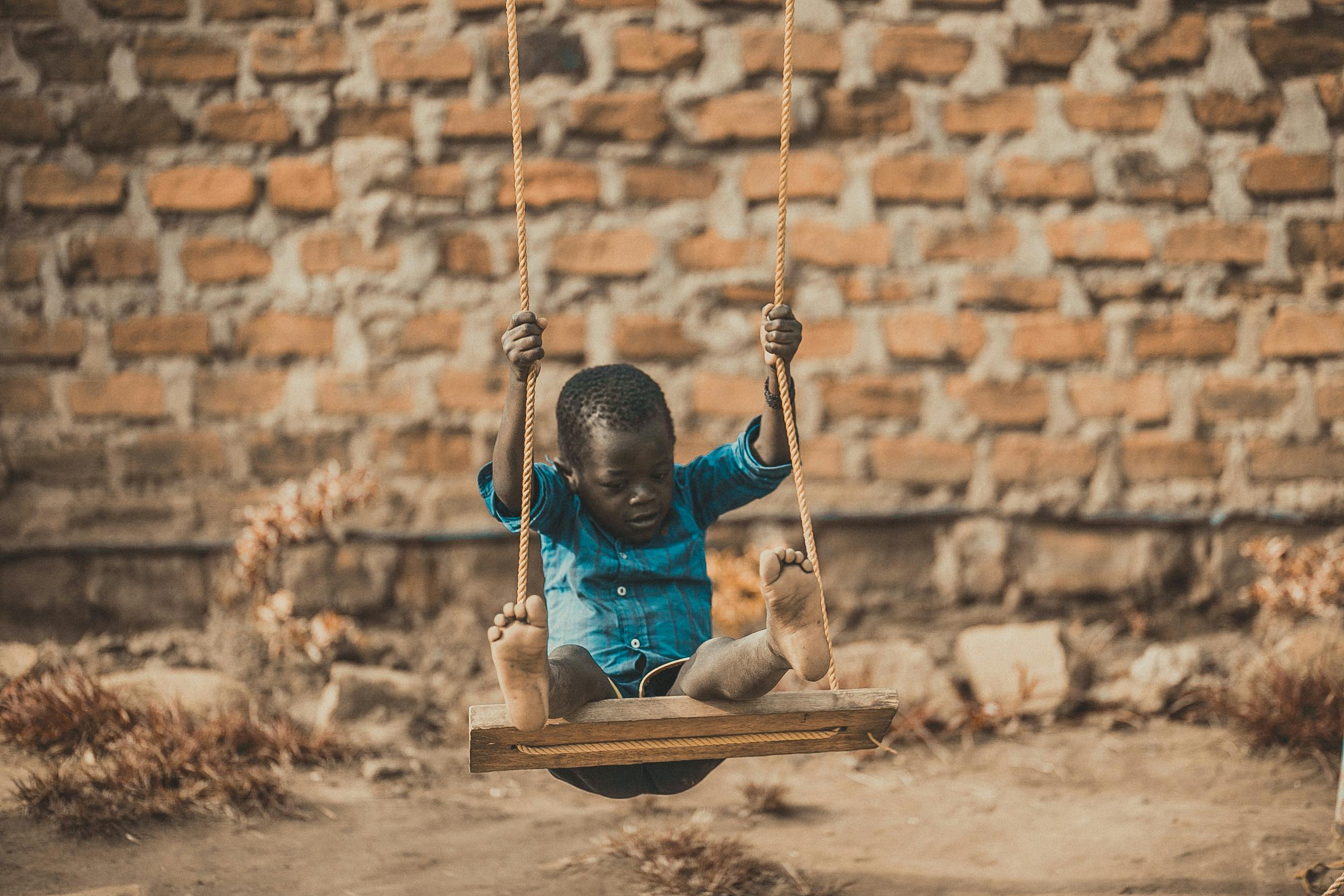 A young boy enjoys a playful moment swinging outdoors in front of a rustic brick wall.